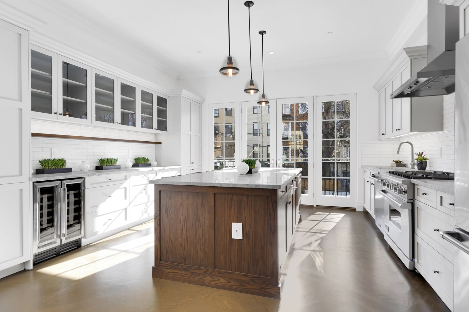 White shaker kitchen with walnut-stained island, wine refrigerator and French doors to a terrace by Gallery KBNY