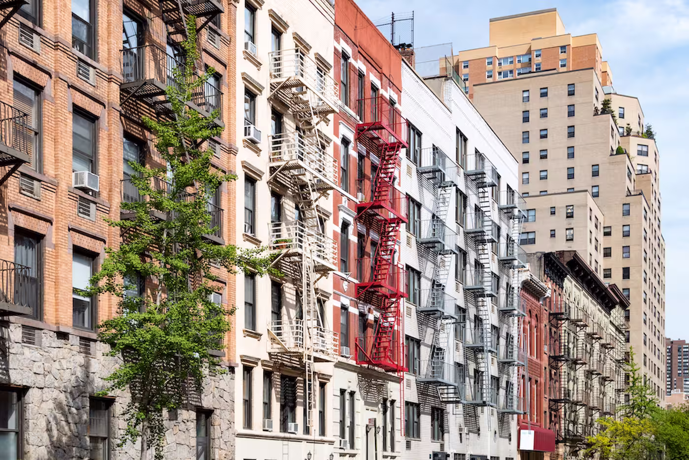 Row of Manhattan apartment buildings with fire escapes along a tree-lined street