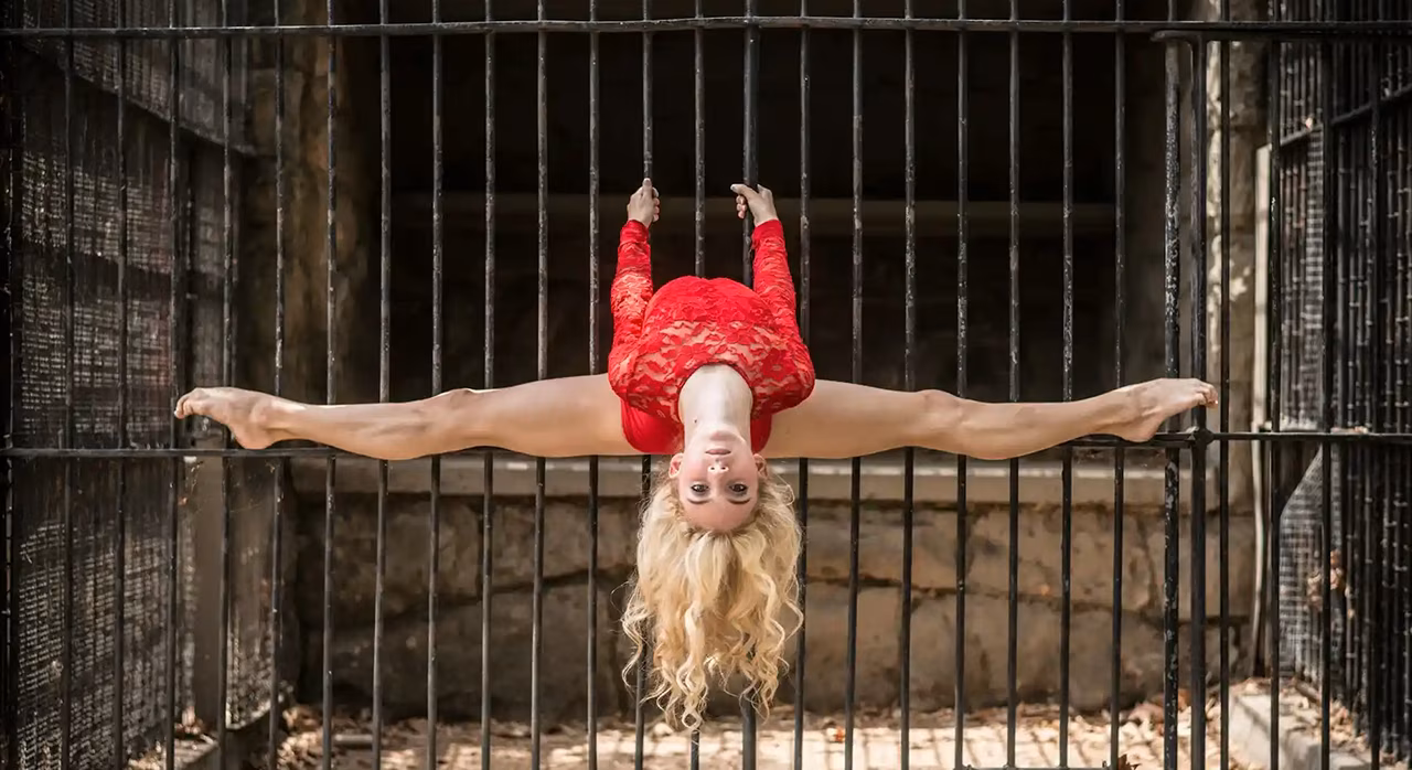 Una mujer de rojo se estira mirando boca abajo sobre una verja metálica.