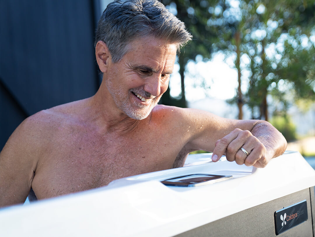 Man bedient Caldera Spas app op smartphone naast zijn spa