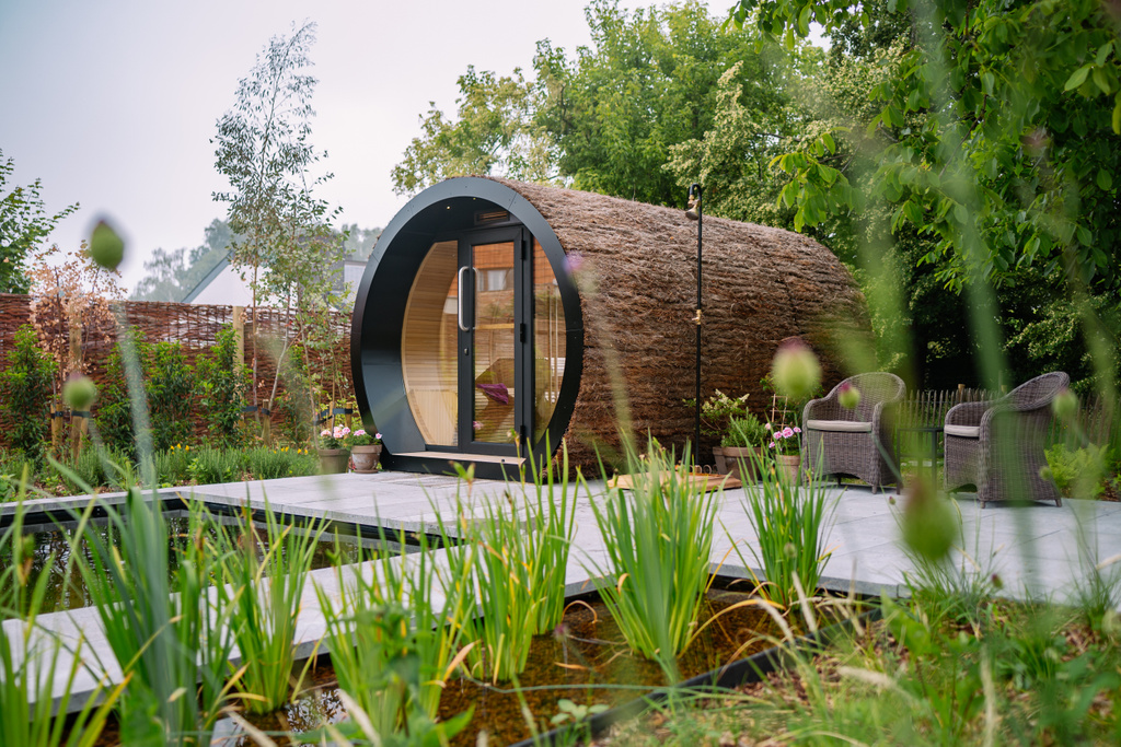 Moderne houten tuinhuisje met rond raam in groene omgeving met waterpartij