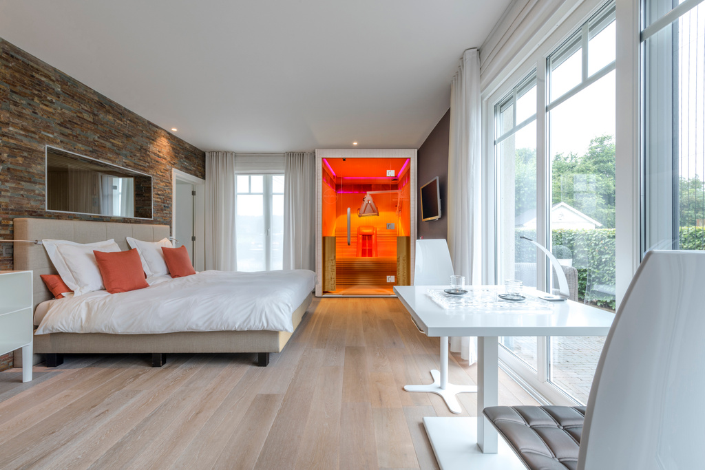 Moderne slaapkamer met wit bed, steenmuur en oranje sauna