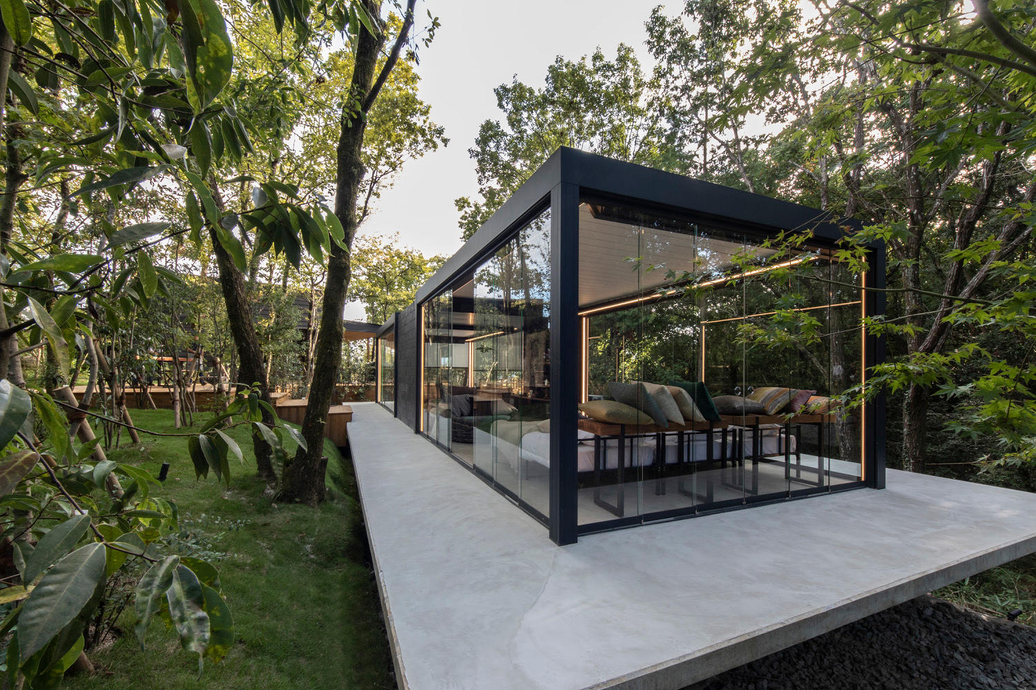 Moderne glazen renson overkapping met zitruimte tussen groene bomen