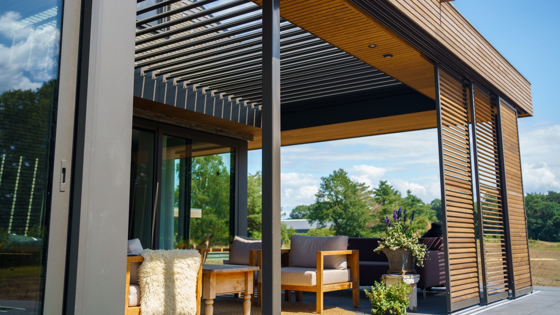 Moderne houten renson overkapping met zithoek en groot raam op zonnige dag