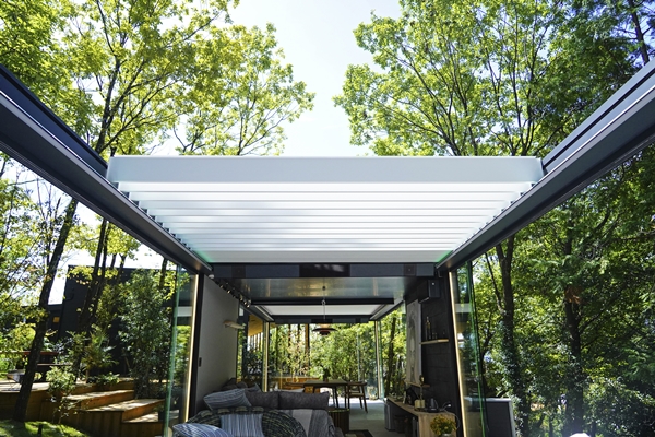 Moderne glazen veranda met Renson-zonwering, omgeven door groene bomen