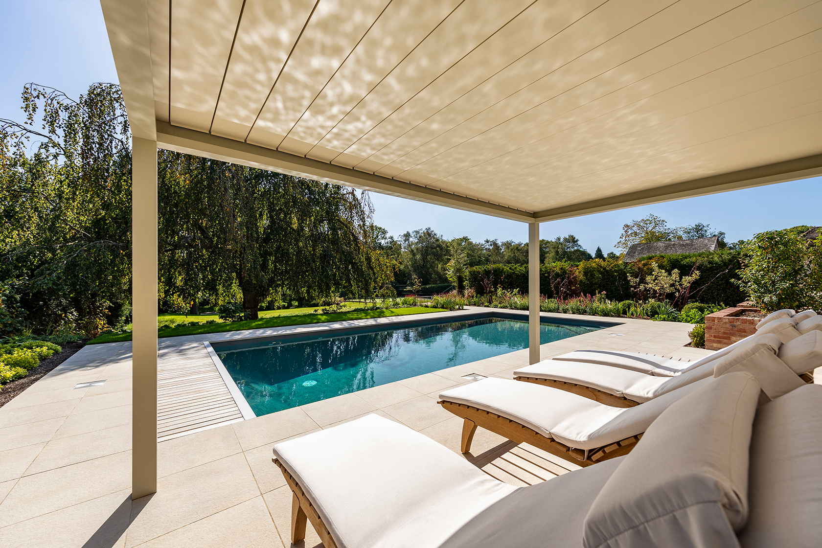 Rustgevend zwembad met ligbedden onder overkapping in groene tuin