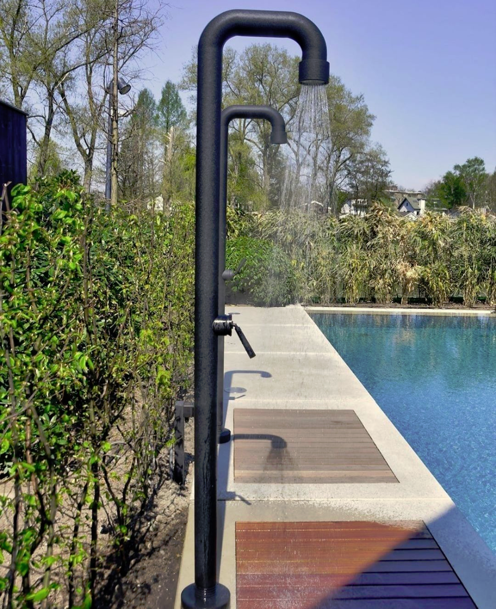 Zwarte buitendouche naast een strak zwembad met groene tuinachtergrond