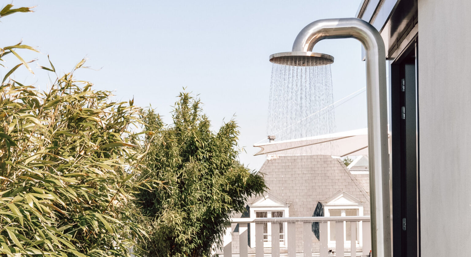 Buitendouche met waterstraal naast groene struiken en wit huis
