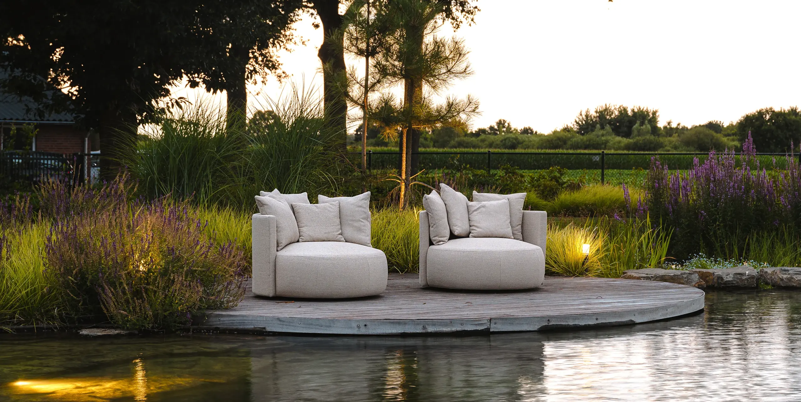 Twee witte loungebanken op een houten terras naast water en lavendel