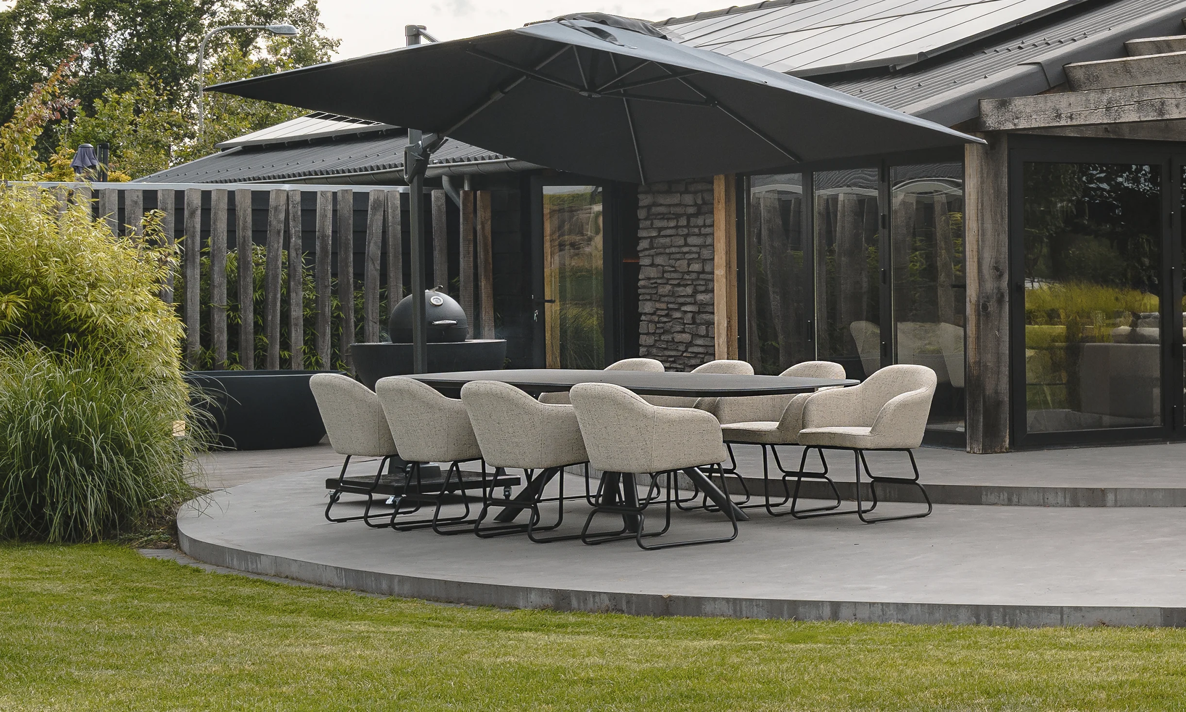 Moderne buiteneetplaats met grijze stoelen onder parasol op betonnen terras