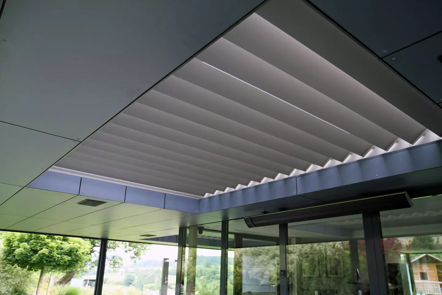 Modern inbouw lamellen dak met gelaagd plafond en zonwering, uitzicht op groene bomen