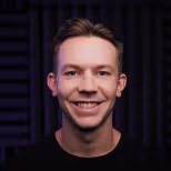 Smiling Matthew Cutler with short brown hair wearing a black shirt against a dark soundproof background.