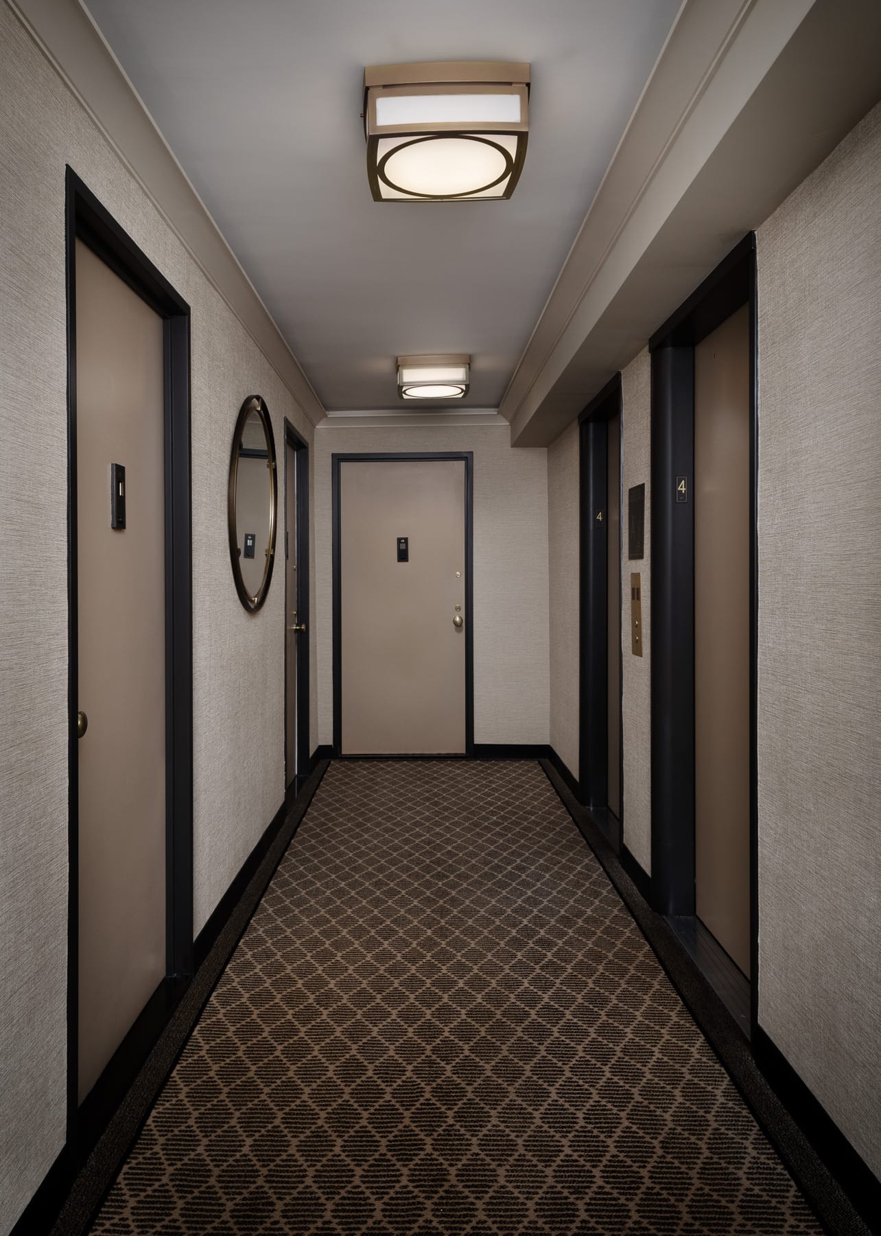 A short elevator lobby on the fourth floor has apartment doors, patterned carpet, a round wall mirror, and two elevator doors.