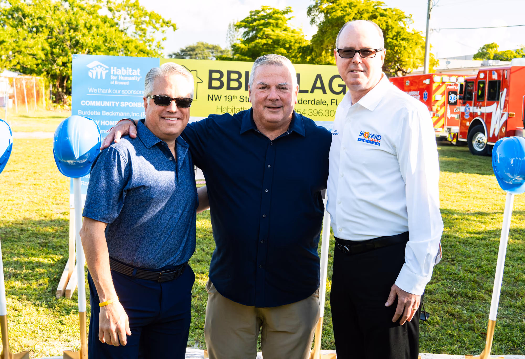 Three attendees in front of the BBI Village project sign
