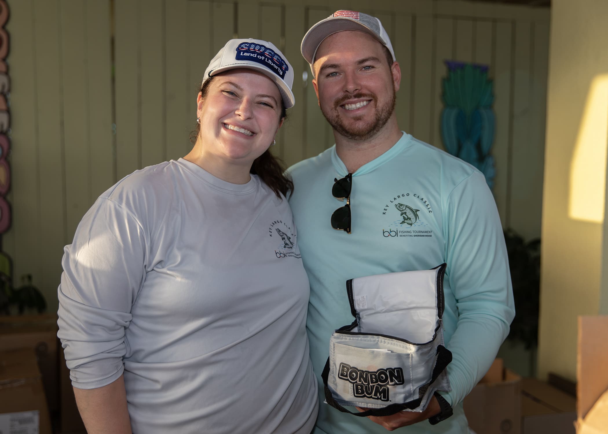 Man and woman in Key Largo Classic tournament shirts holding a "Bon Bon Bum" cooler bag.