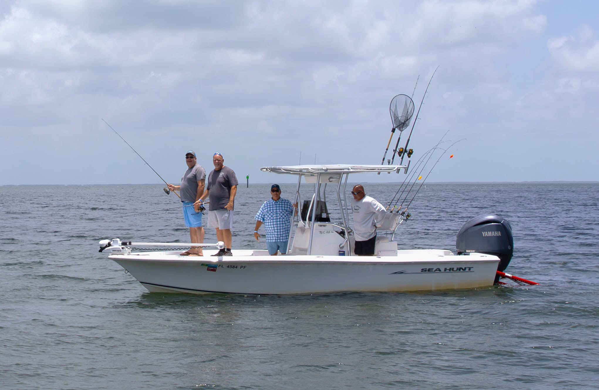 Fishing boat with multiple rods and three anglers on open water.