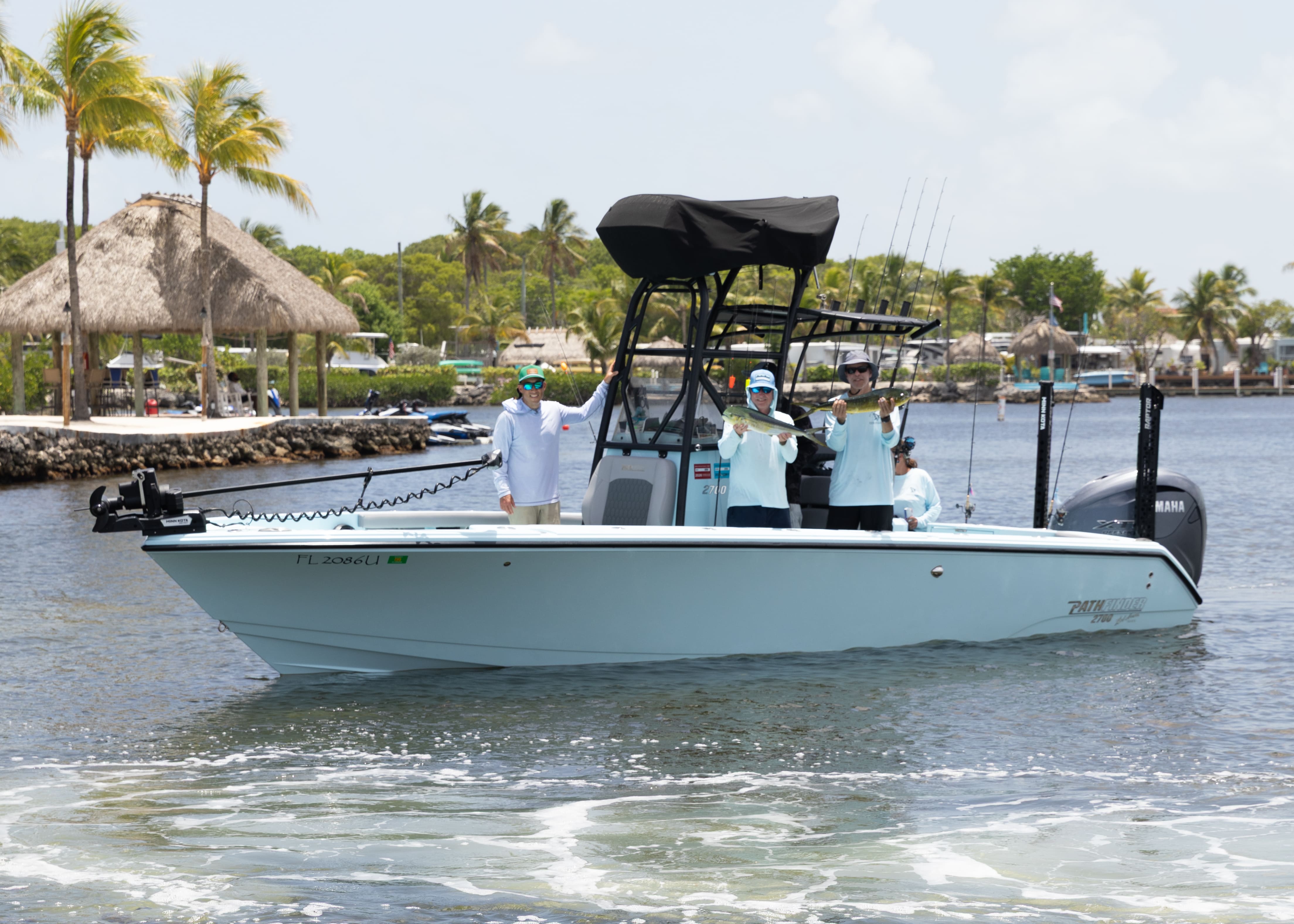 Fishing boat with several anglers aboard cruising past a waterfront tiki hut.