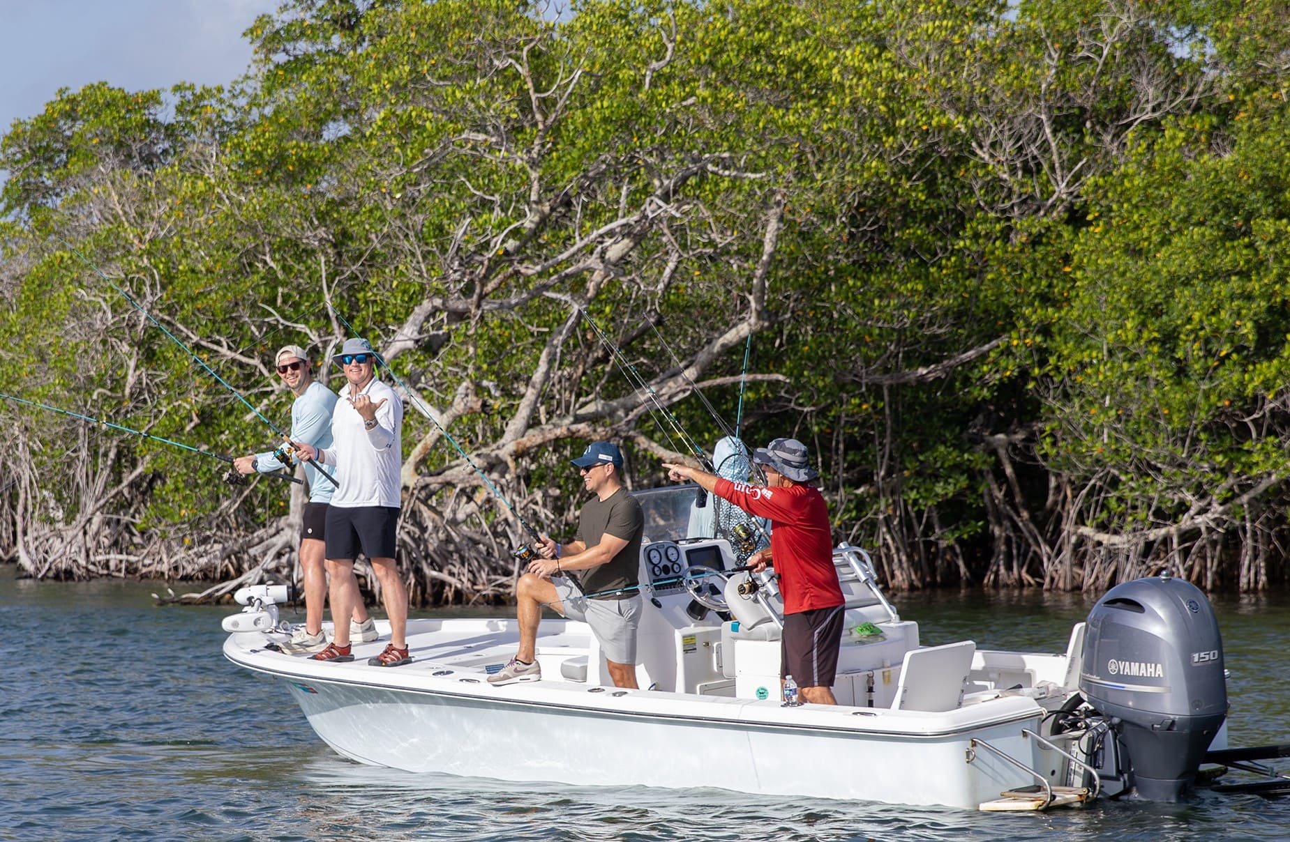Anglers on a boat near mangroves, one team member pointing toward the water during the fishing tournament.