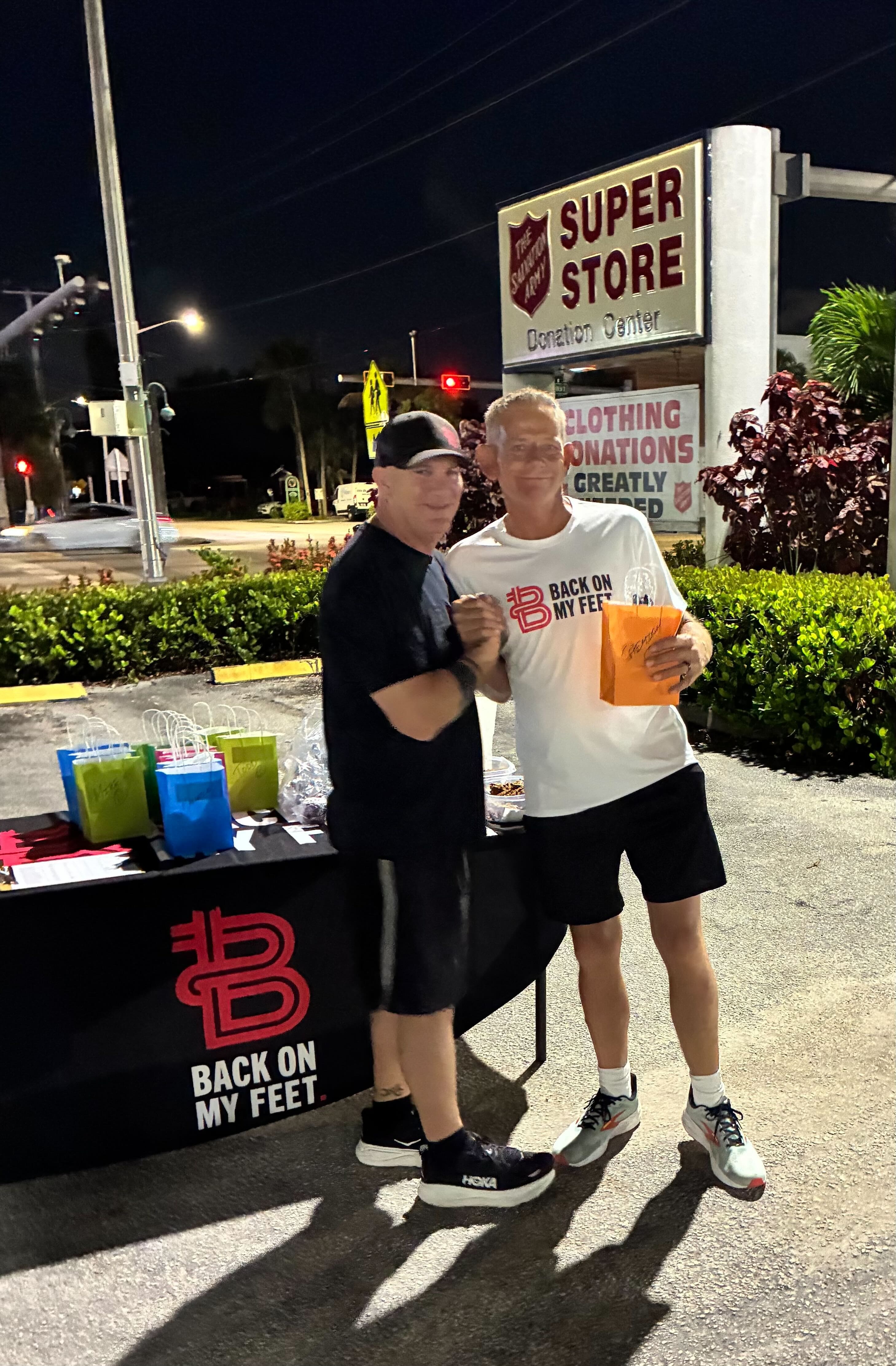 Two men presenting an award at a Back on My Feet branded table outdoors at night