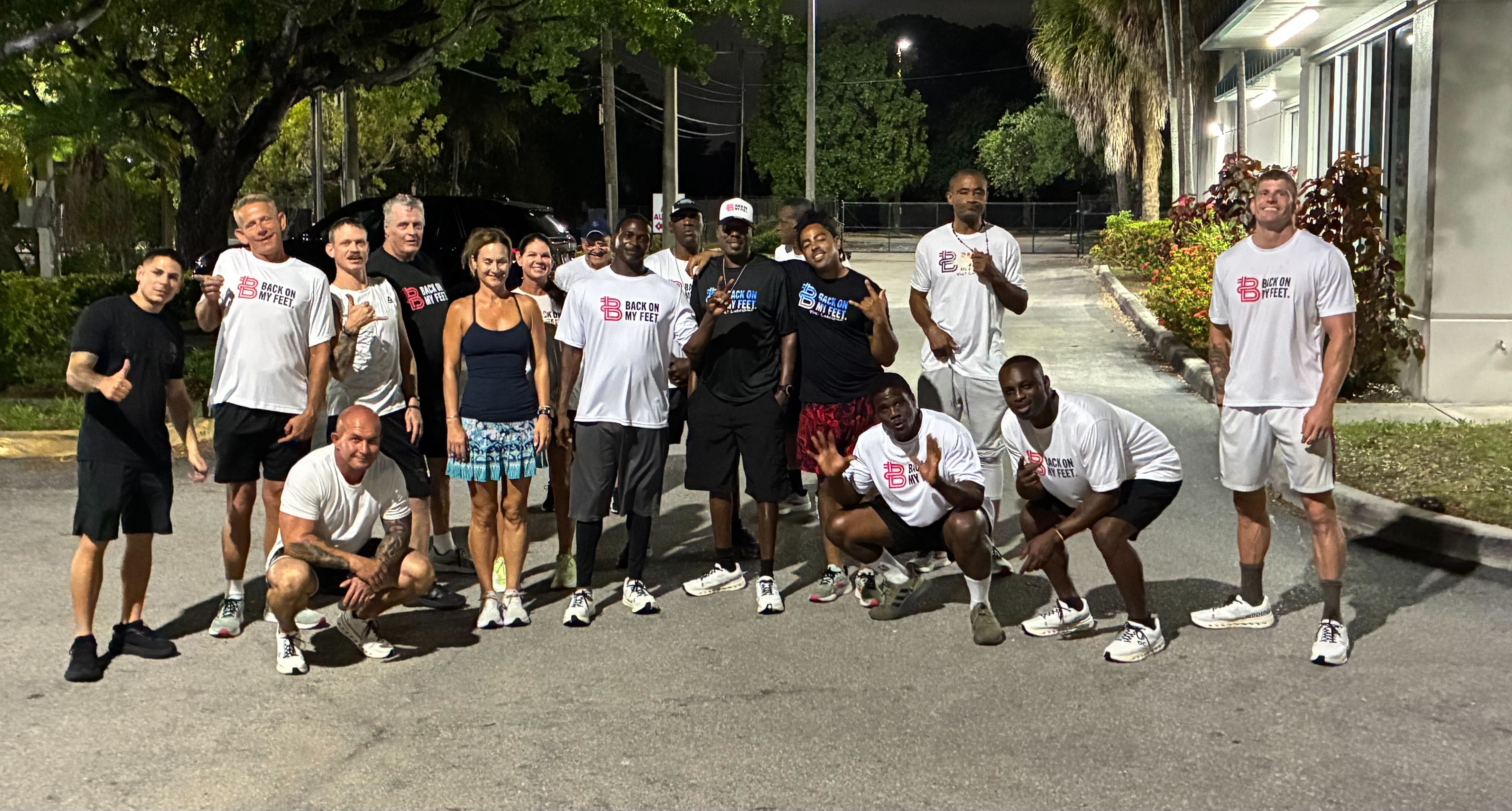 Group of Back on My Feet members posing together outdoors at night, including a woman in pink shorts