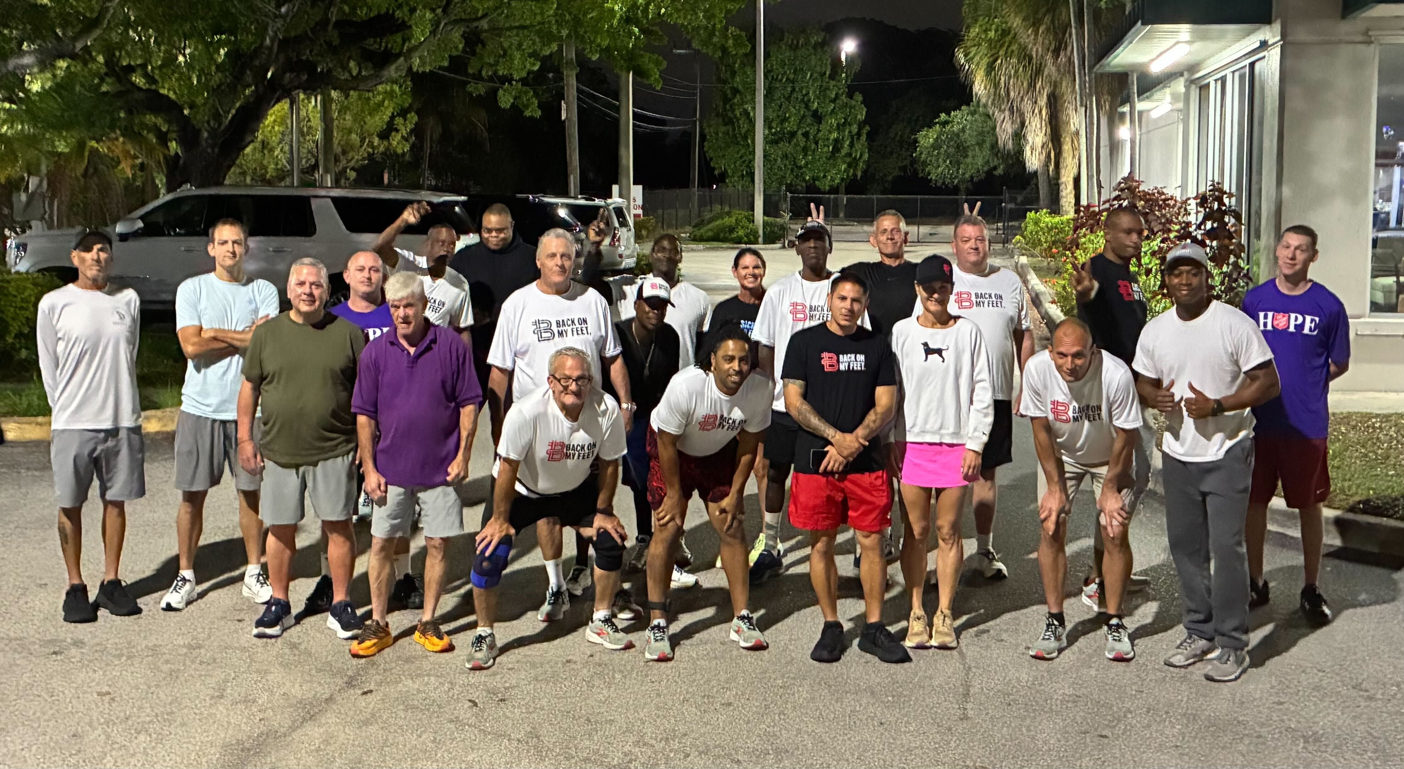 Group of Back on My Feet members posing together outdoors at night, one member wearing red shorts