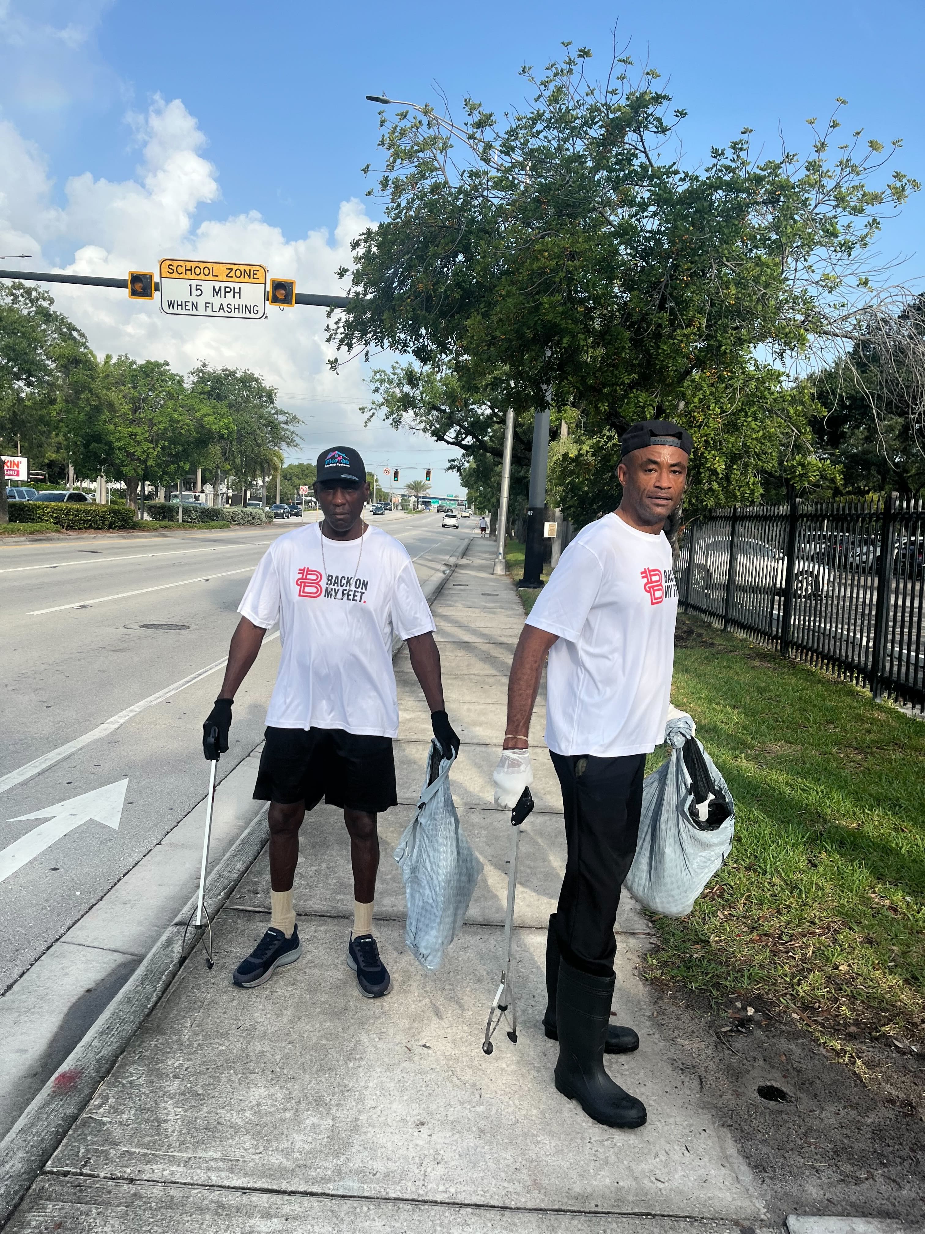Back on My Feet member standing on a road holding trash bags during a daytime community clean up