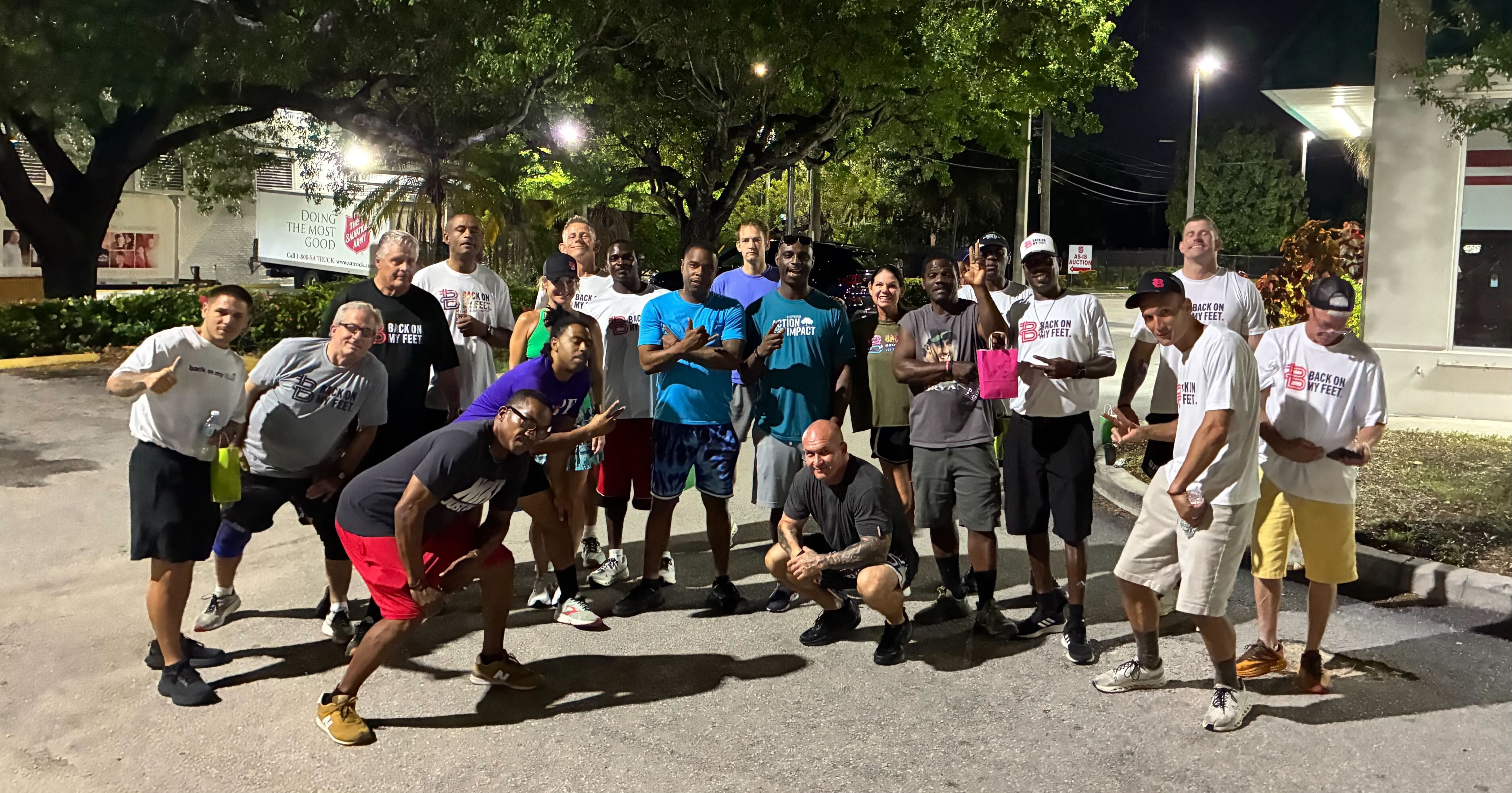 Group of Back on My Feet members in blue and black shirts posing together outdoors at night