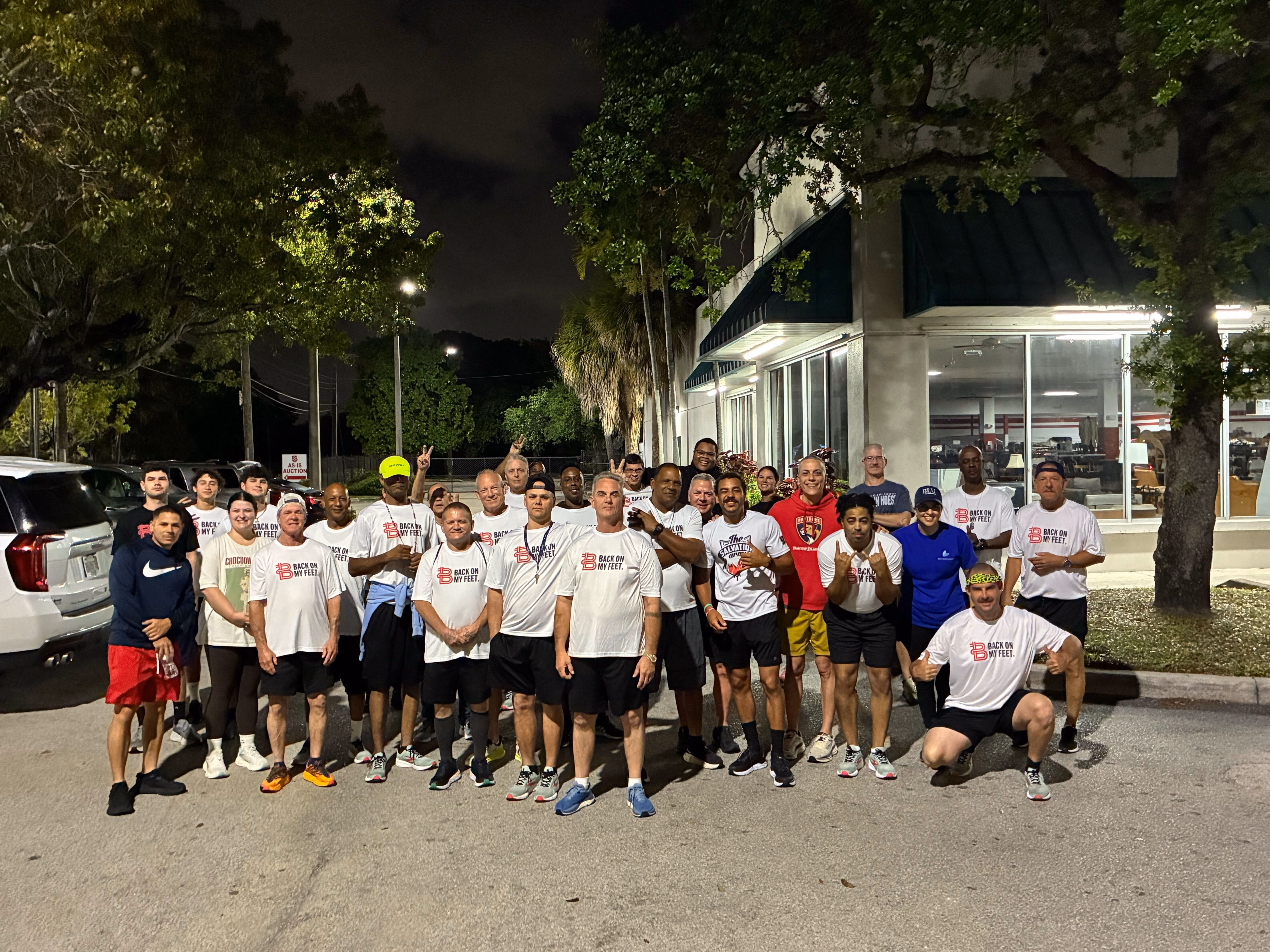 Group of Back on My Feet members in white shirts posing together outdoors at night