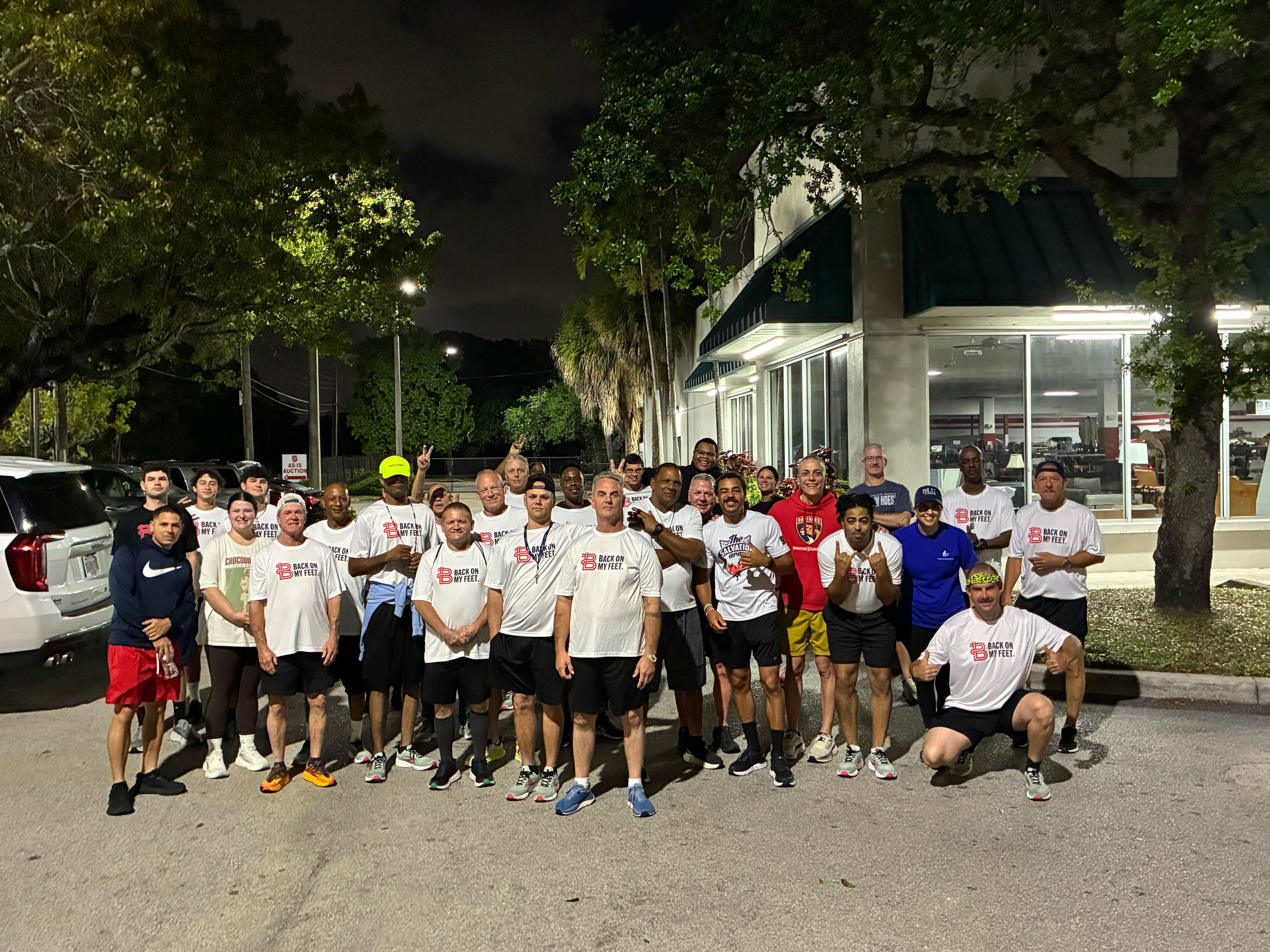 Group of Back on My Feet members in white shirts posing together outdoors at night