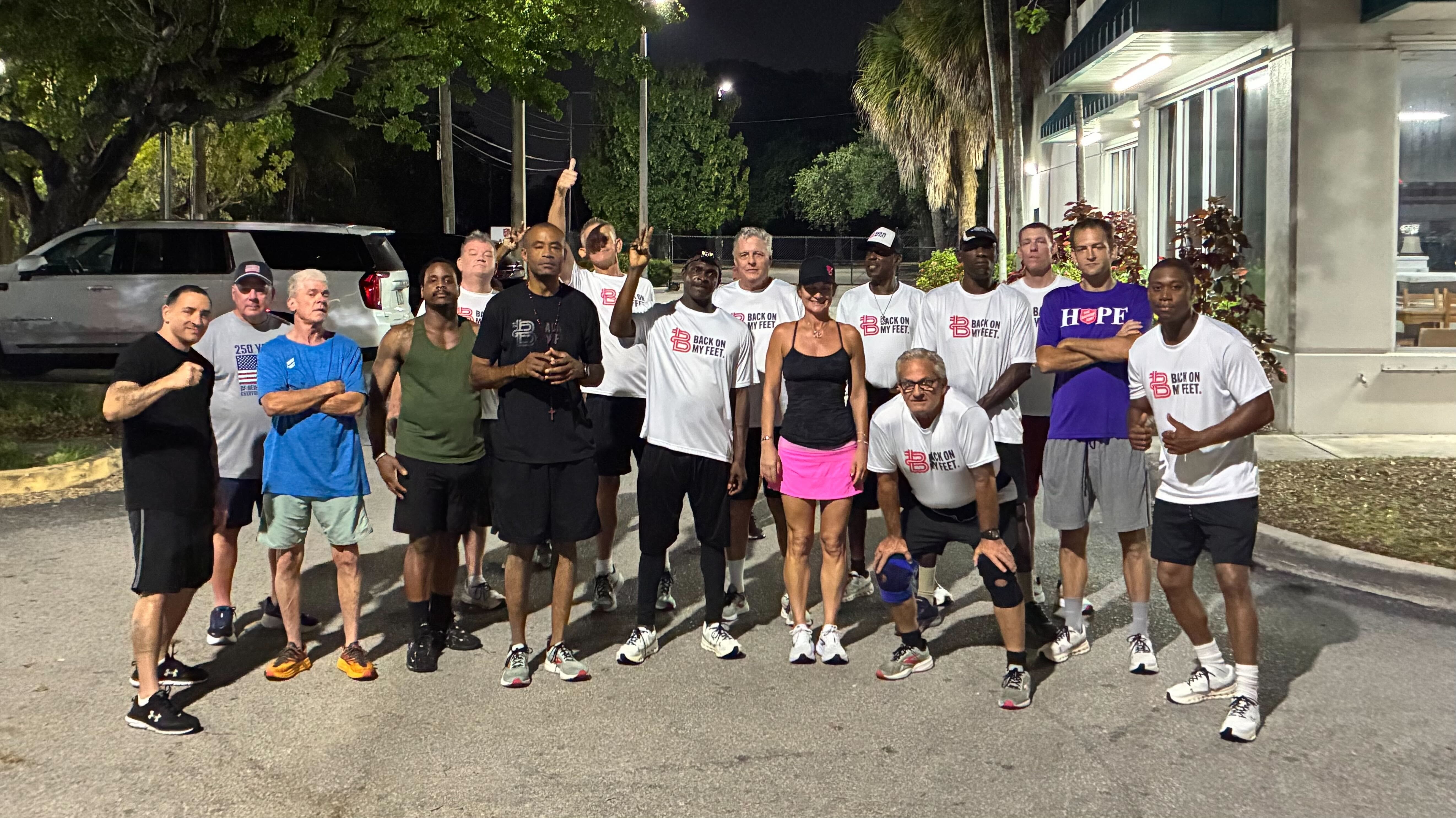 Group of Back on My Feet members posing together outdoors at night, including a woman in pink shorts