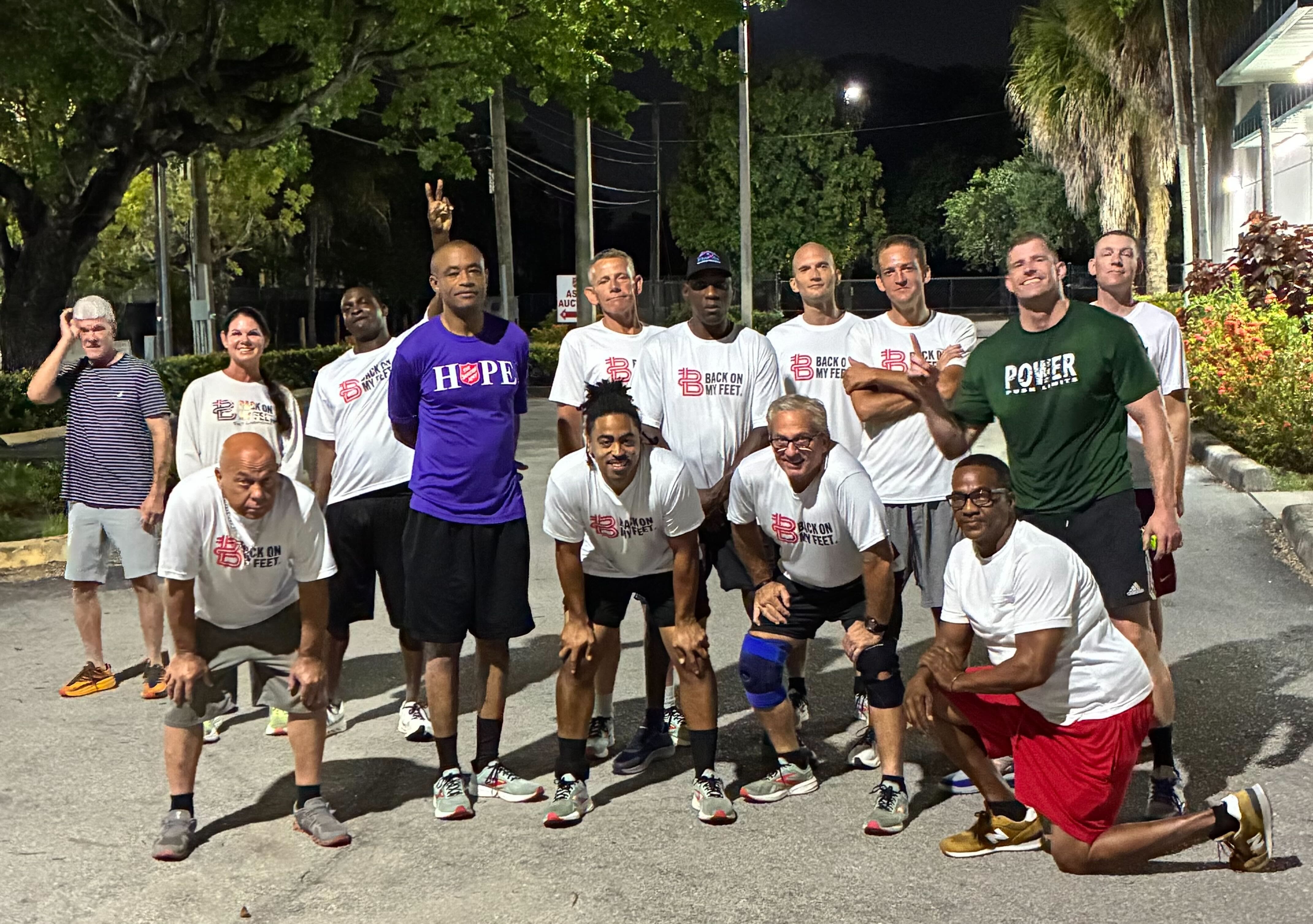 Group of Back on My Feet members in purple and black shirts posing together outdoors at night