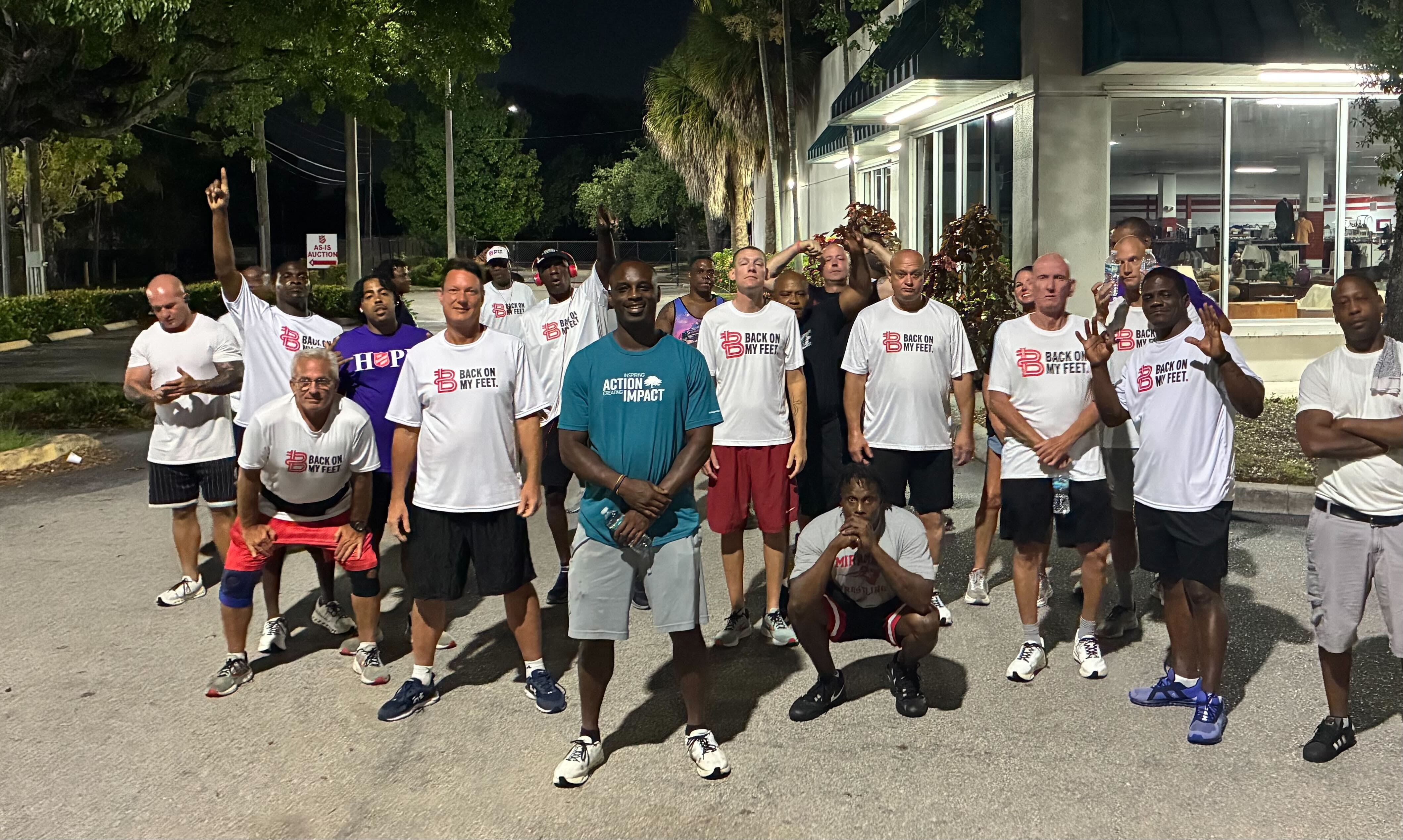 Group of Back on My Feet members posing together outdoors at night, one wearing a teal shirt