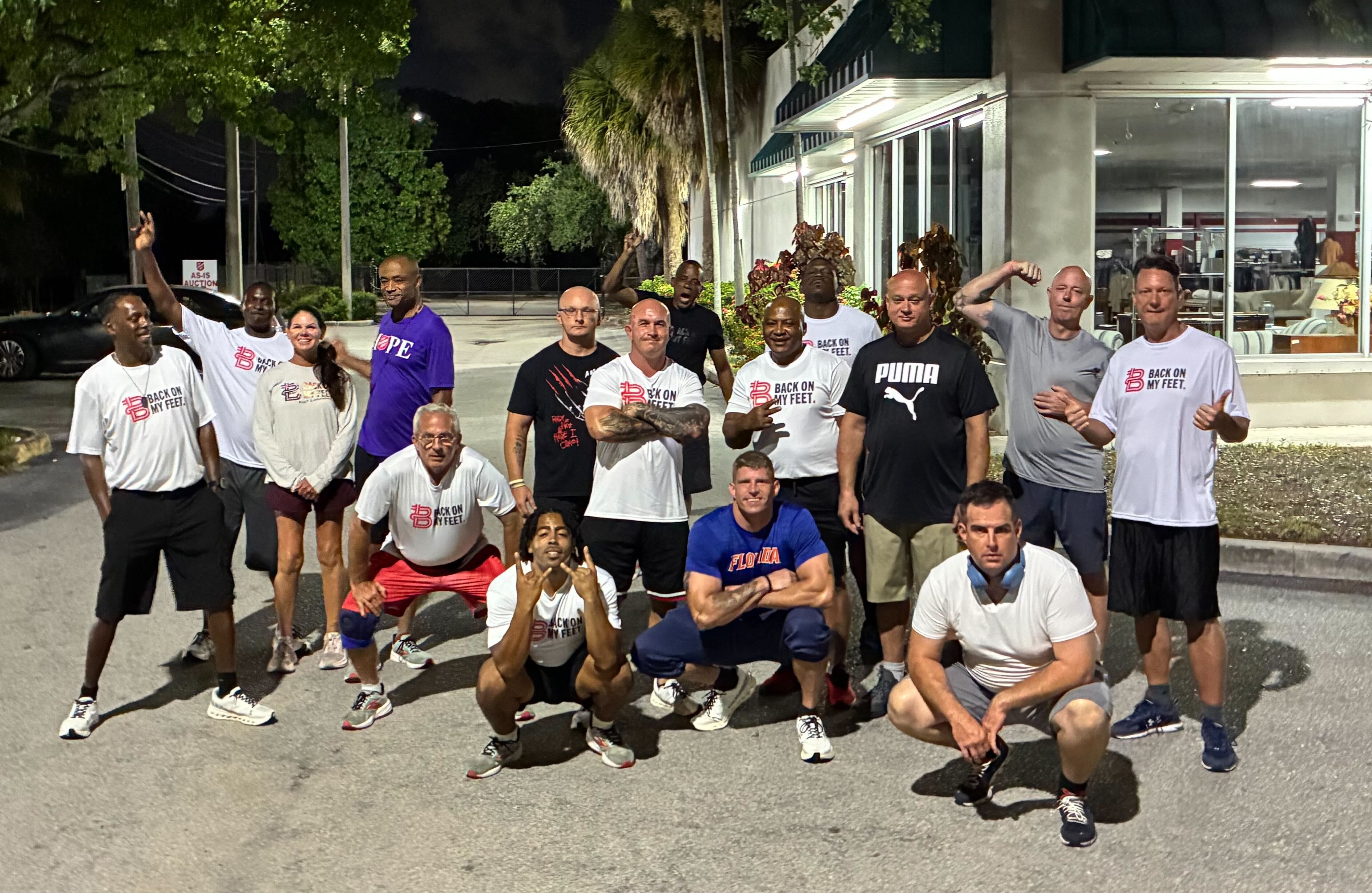Group of Back on My Feet members posing together outdoors at night, one member raising a fist