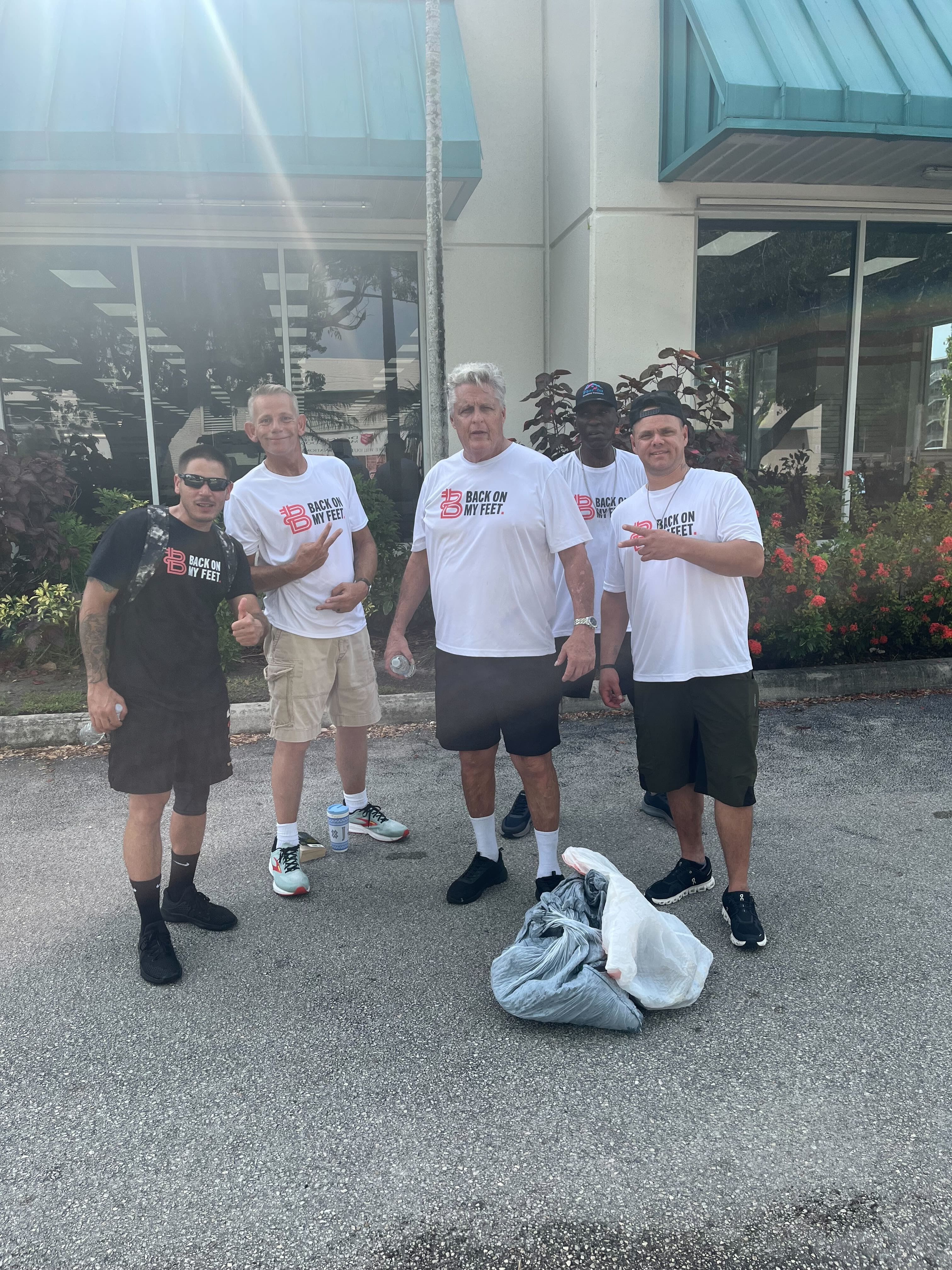 Two Back on My Feet members standing together at night beside a bag of trash collected during a clean up