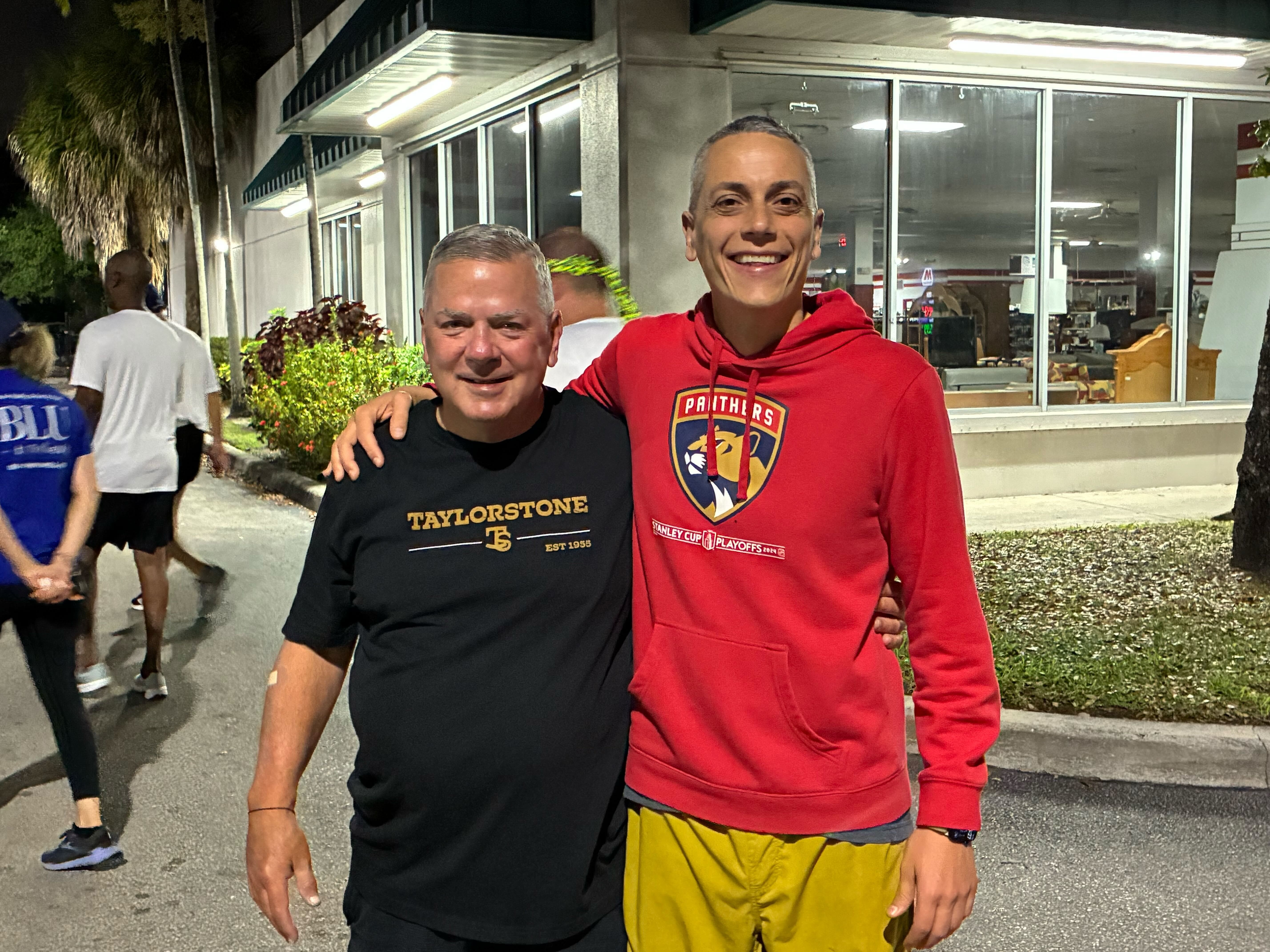 Two men smiling together, one wearing a Back on My Feet cap and the other a red hoodie