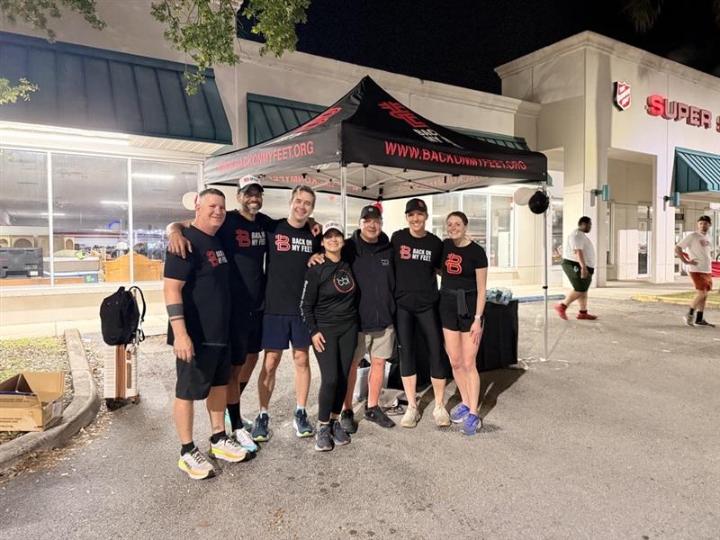 Runners posing in front of a black event tent outside a store