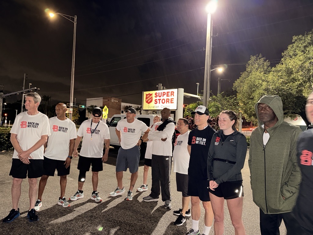 Runners in white Back on My Feet shirts lined up in a parking lot at night