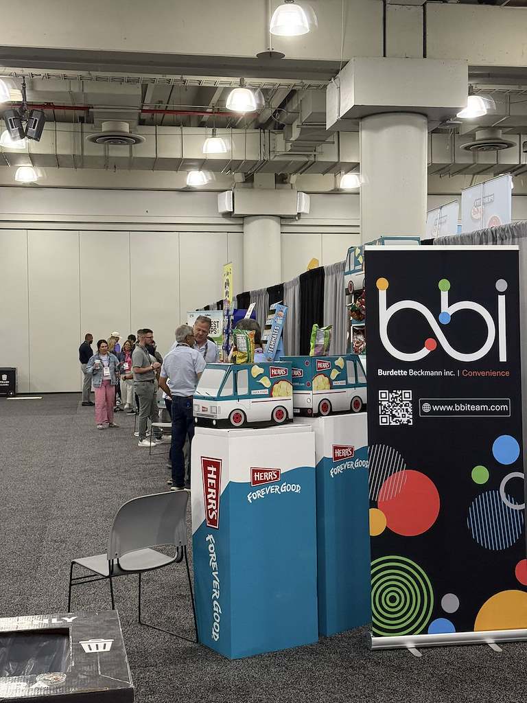 Trade show aisle with a bbi Burdette Beckmann Convenience banner beside Herr's displays shaped like delivery vans.