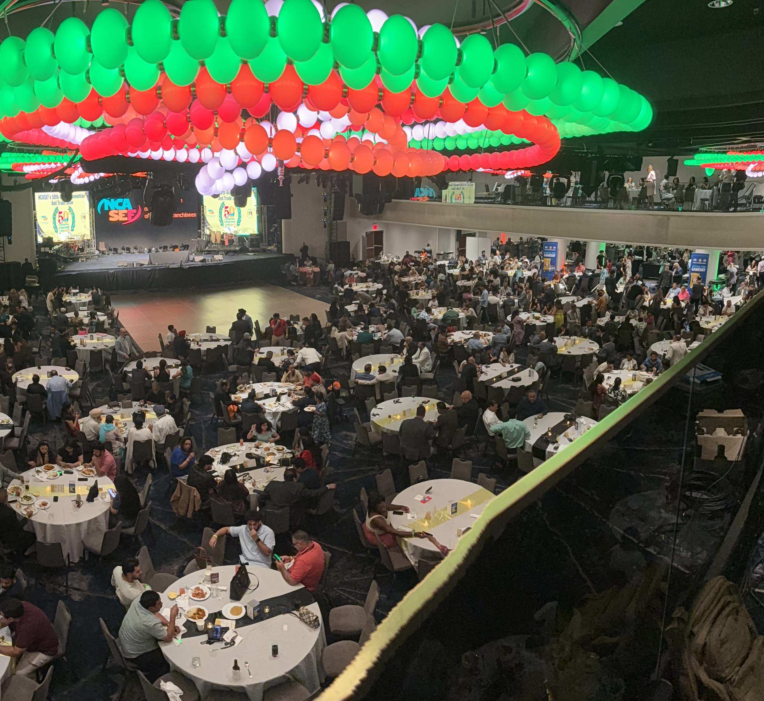 Banquet hall from above, red and green balloon ceiling over crowded dining tables and a stage.