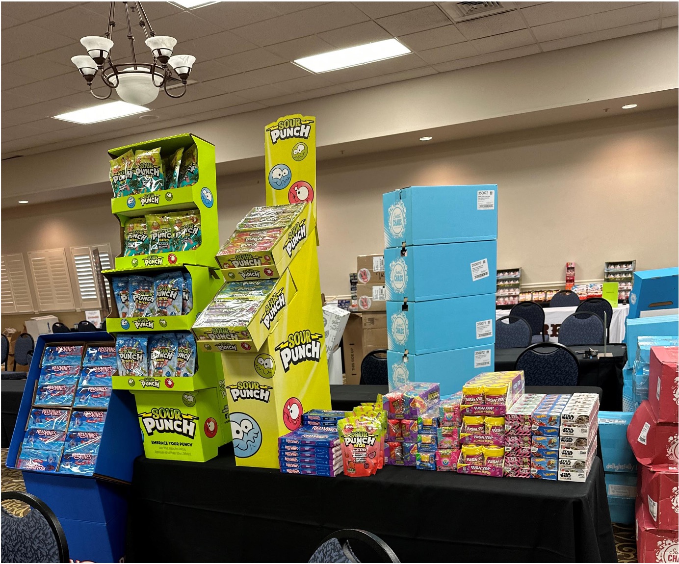 Yellow Sour Punch displays, blue candy cartons and boxed candy on a black-draped table in a ballroom.