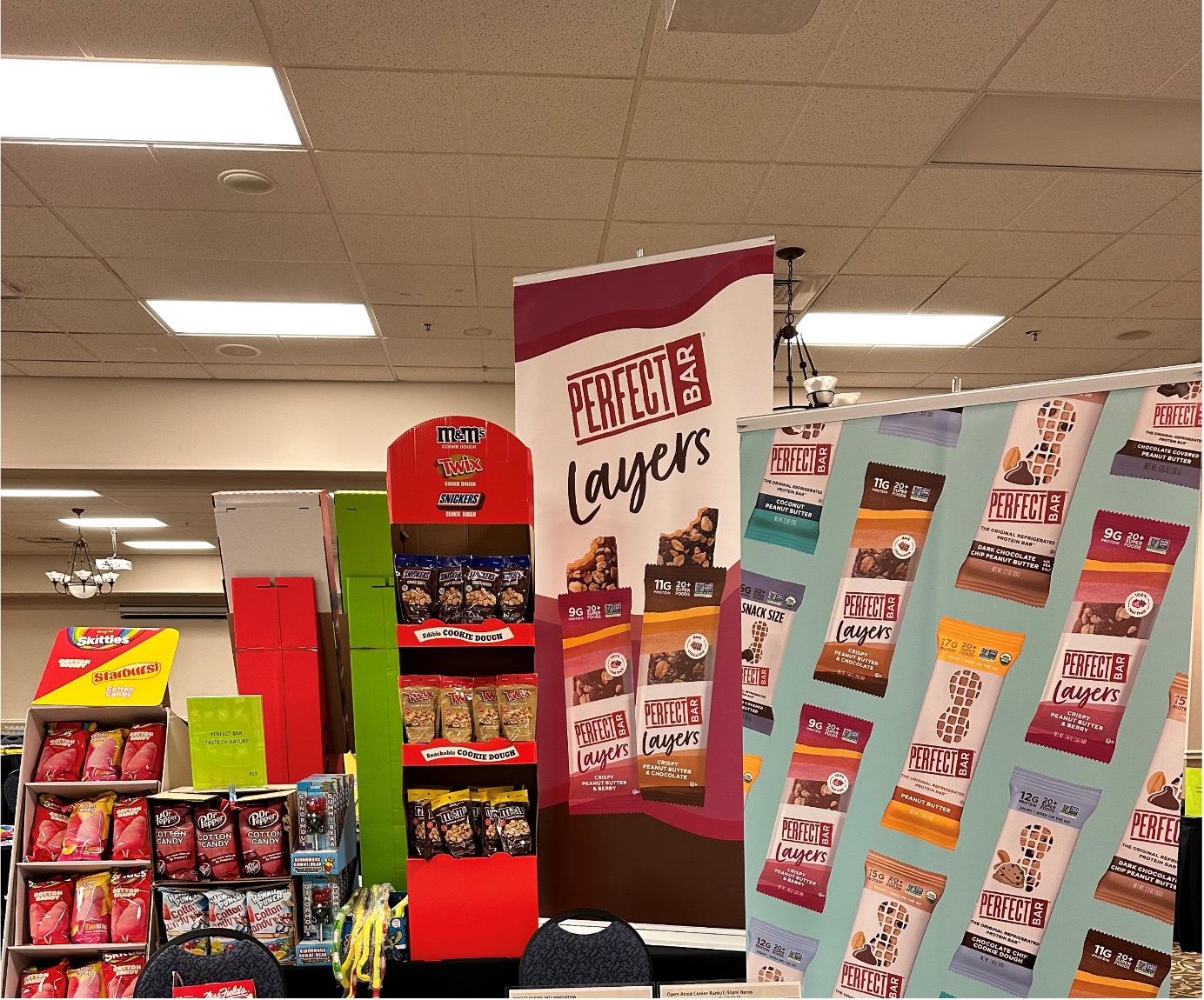 Perfect Bar Layers banners beside a red M&M's display rack, with Skittles and Dr Pepper cotton candy displays.