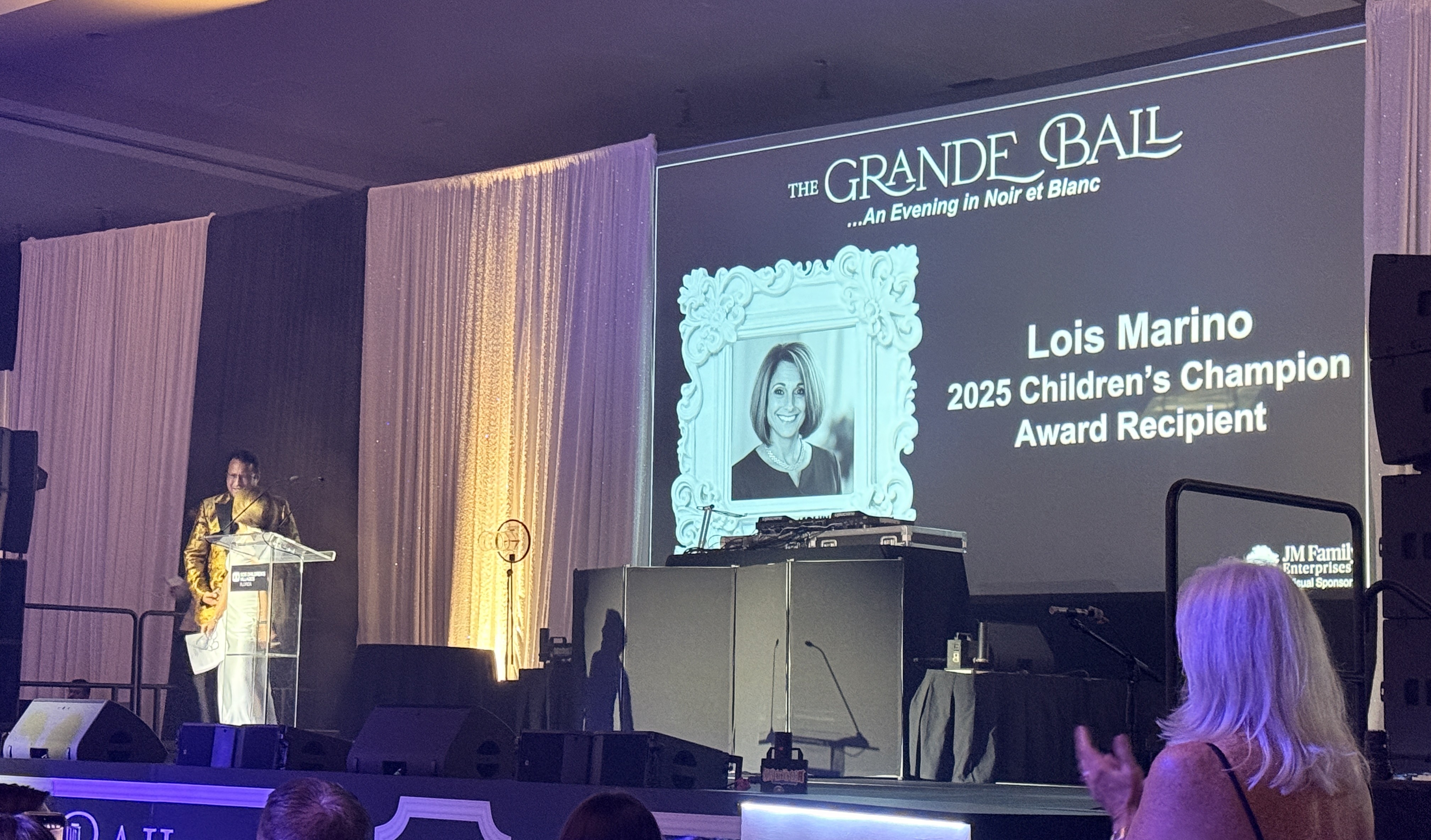 Person at a podium beside a screen reading Lois Marino, 2025 Children's Champion Award Recipient.