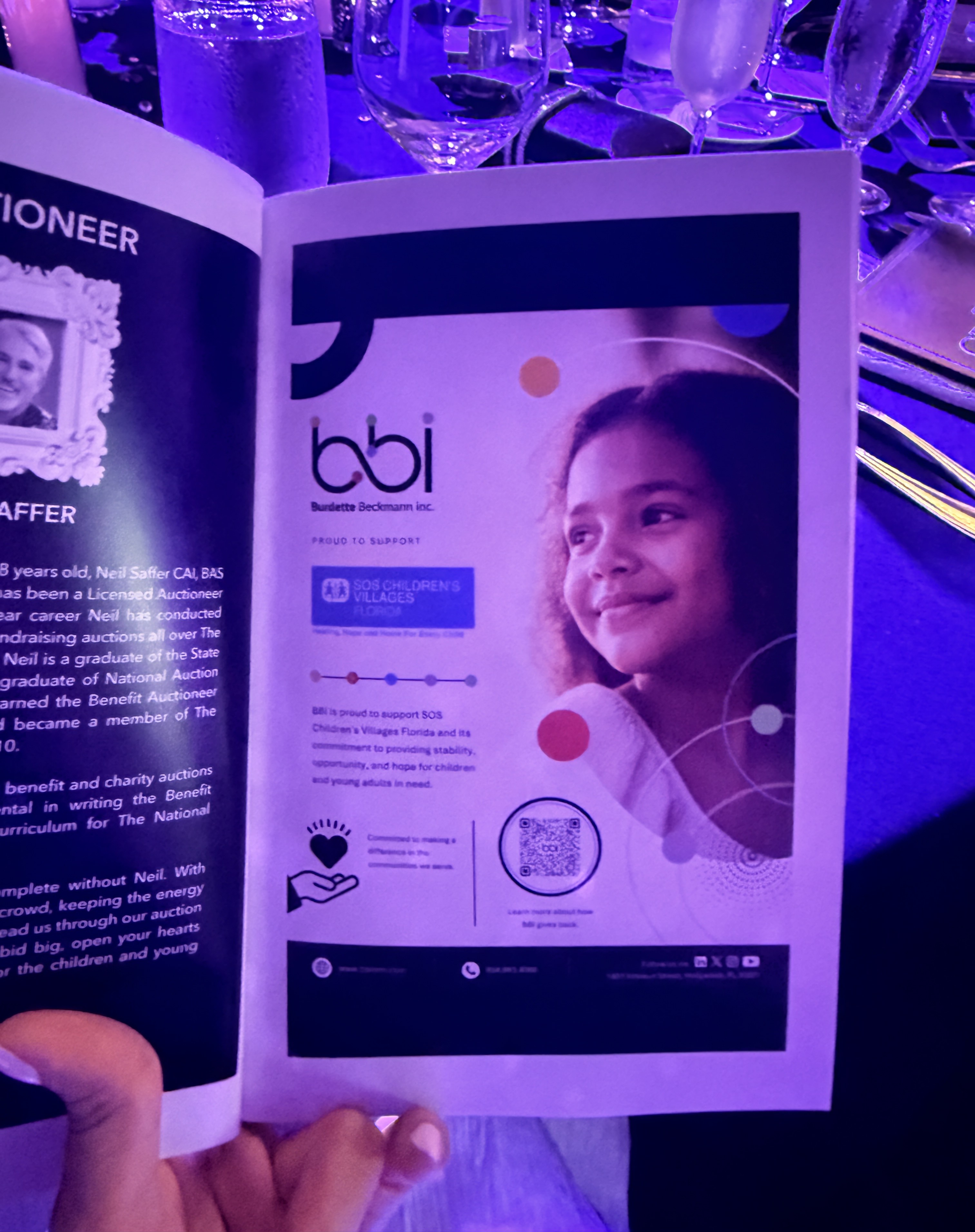 Hand holding an open event program to a bbi ad supporting SOS Children's Villages Florida, with a smiling girl.