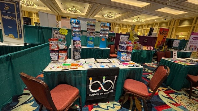bbi booth table with Welch's fruit snack displays, an Eagle 20's sign at left and empty chairs in a ballroom.