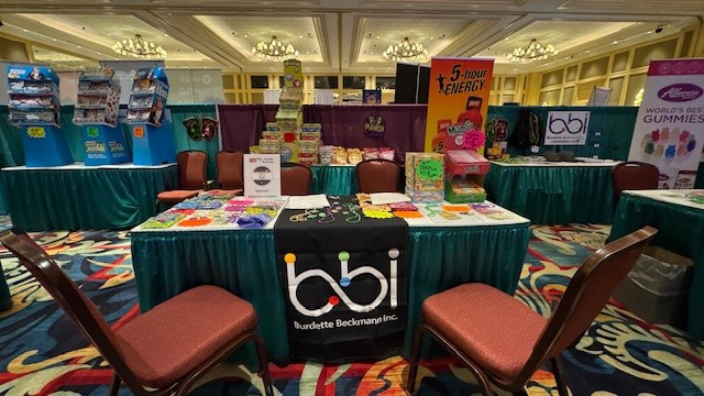 bbi booth table with candy and bead necklaces beneath a 5-hour ENERGY banner in an empty ballroom.
