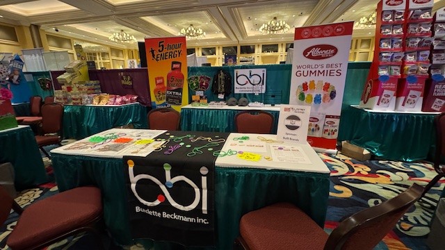 bbi booth table with beads and price sheets, with 5-hour ENERGY and Albanese gummies banners and a bbi sign behind.