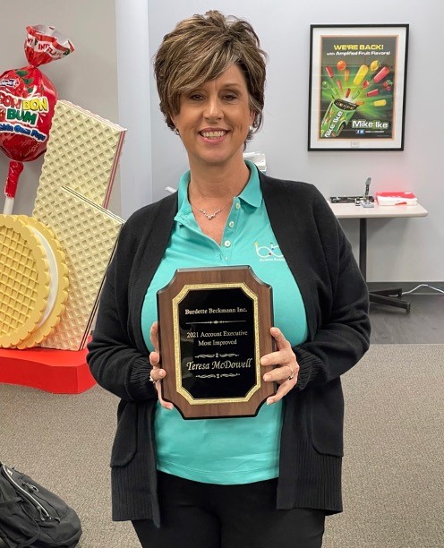 Woman in a teal BBI polo and black cardigan holds a plaque reading 2021 Account Executive Most Improved, Teresa McDowell.