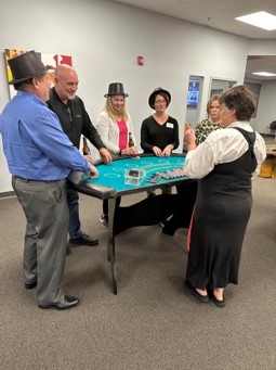 Players, some in black hats, lean in at a teal casino table as a dealer in a black apron stands at its end.