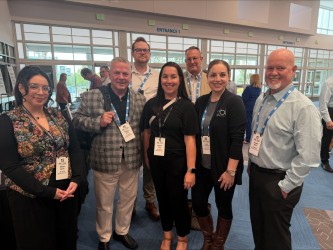 Group of adults wearing conference lanyards poses together in a convention lobby.