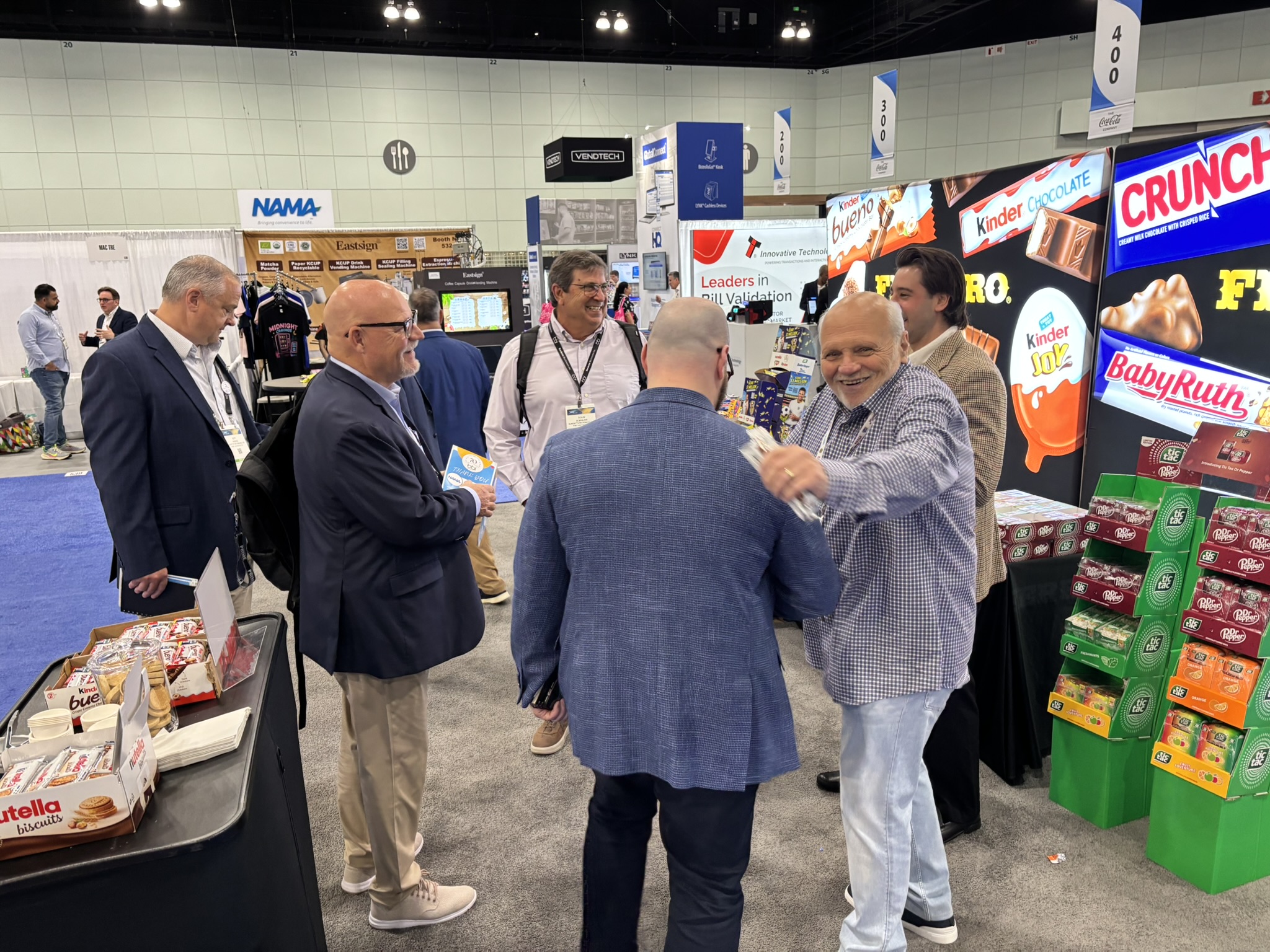 Attendees chat in a trade show aisle beside a Ferrero booth with Kinder, Crunch and Baby Ruth displays.